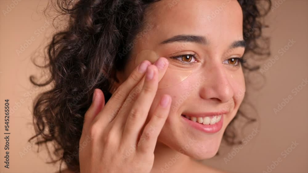 A young caucasian smiling woman placing patches under her eyes. Slow motion A young caucasian smiling woman placing patches under her eyes. Slow motion