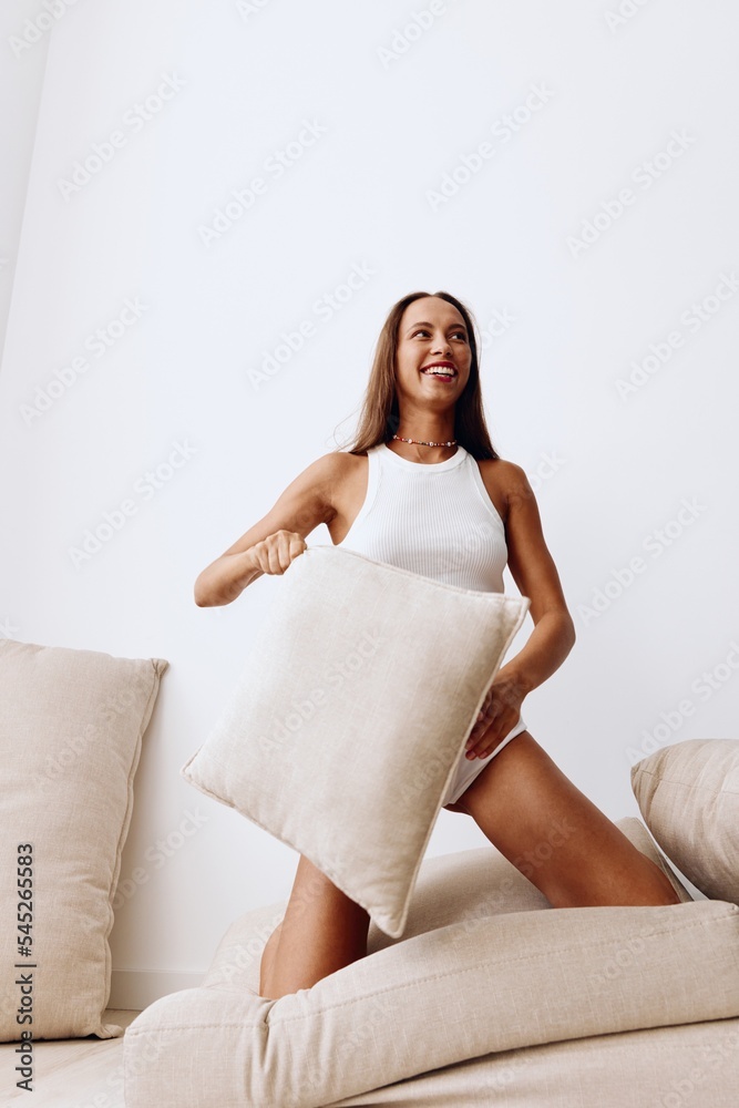 Beautiful woman in home lingerie plays with pillows from the couch throws up with a smile and has fun. Lifestyle in a happy home and fun time Beautiful woman in home lingerie plays with pillows from the couch throws up with a smile and has fun. Lifestyle in a happy home and fun time