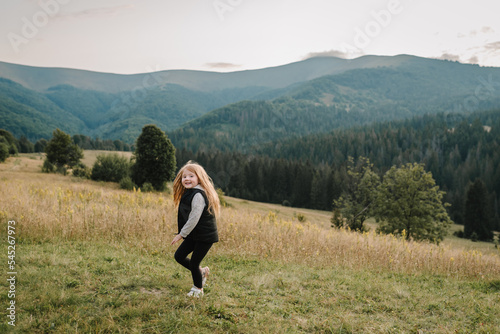Little hiker girl running on grass in autumn mountains. Travel concept. Holiday, trip and vacation. World Tourism Day. Enjoying time kid walk on sunset on top of foggy mountain. Active outdoor games. © Serhii