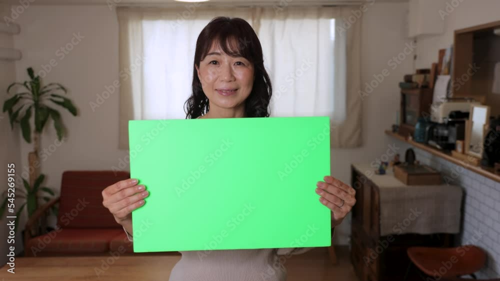 Middle aged asian woman holding green board and smiles. For chromakey editing. Middle aged asian woman holding green board and smiles. For chromakey editing.