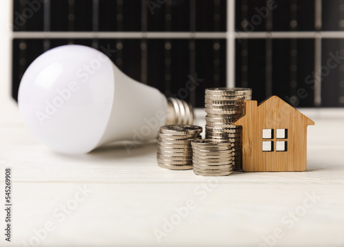 Flat lay composition with solar panel, led lamp, house model and money on  table. Money saving and clean energy concept. Ecology and sustainable development concept. photo