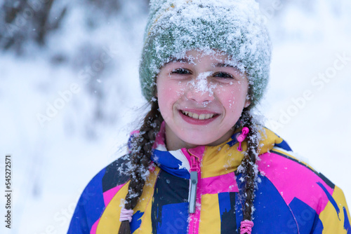 Cute happy smiling little girl, whose face is covered in snow, is enjoying winter
