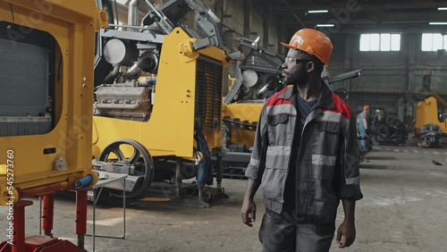 Wallpaper Mural Professional African American male worker in coverall, safety glasses and hard hat walking along tractor production plant looking at vehicle examples Torontodigital.ca