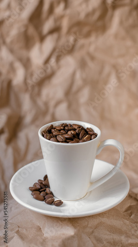 Coffe beans inthe small white cup with saucer on crumpled craft paper background