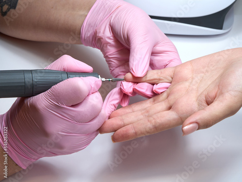 During a manicure, a manicurist buffs off nail polish with an electric nail file. Close up photo