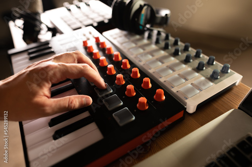 Recording studio, music studio. Musician's hand on the keys of a midi keyboard. Professional musical equipment. Sound work, podcast. Close-up. Low angle view.