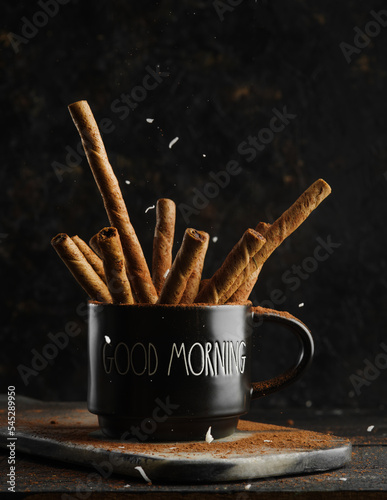 Black coffee cup with fragrant cinnamon sticks on a black background. Hot drinks, alcohol, aromatic spices and seasonings for drinks, confectionery.