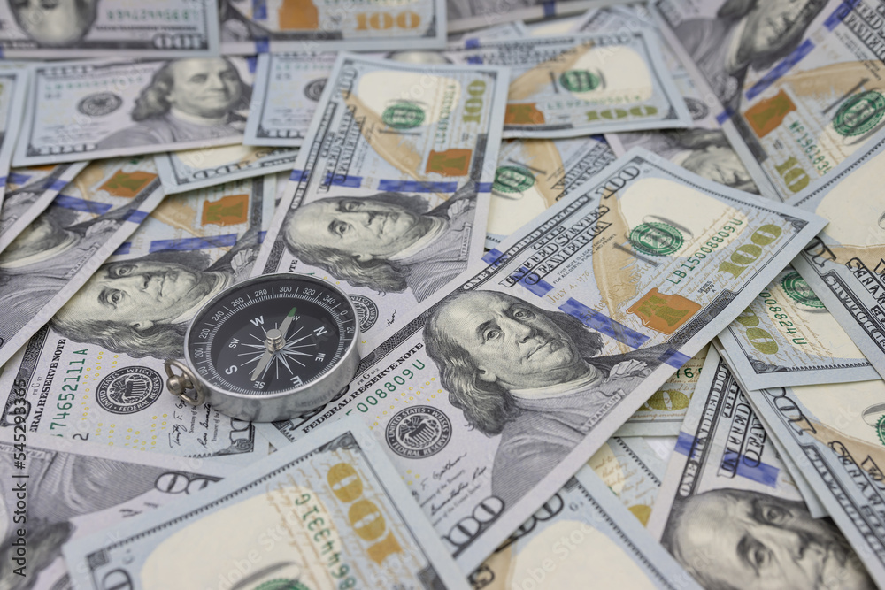 Classic navigational compass on the background of one hundred dollar bills Classic navigational compass on the background of one hundred dollar bills