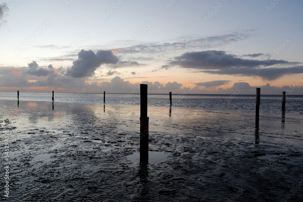 North Sea beach with tides, breakwaters, groynes and pastel sunset, Norddeich Ostfriesland Germany.