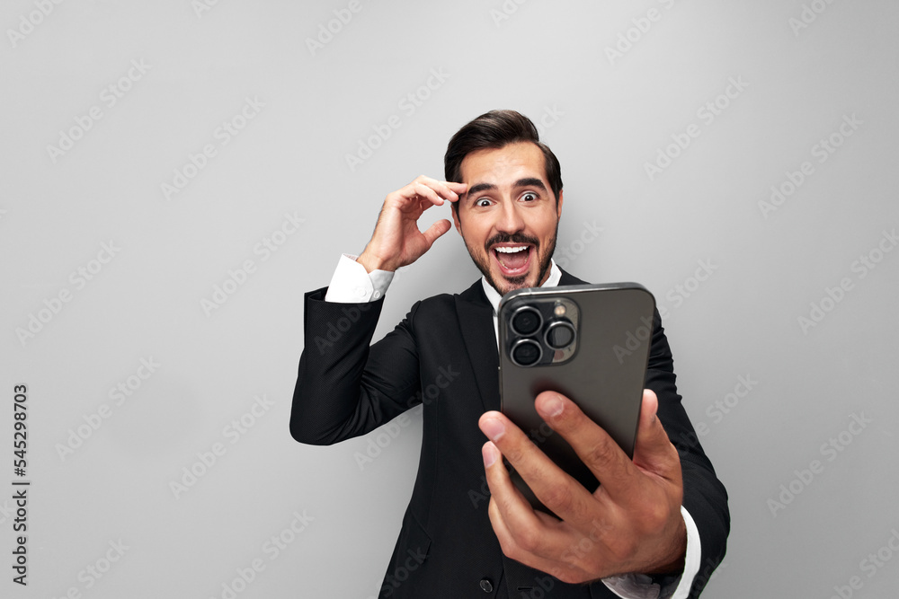 Man businessman in suit holding phone in hand on phone posing in front of smartphone camera with smile with teeth happy surprise win on gray background close-up face wide camera angle, technology Man businessman in suit holding phone in hand on phone posing in front of smartphone camera with smile with teeth happy surprise win on gray background close-up face wide camera angle, technology