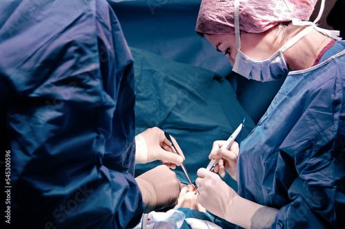 Surgeon and his assistant performing cosmetic surgery in hospital operating room. Surgeon in mask wearing loupes during medical procadure. Breast augmentation, enlargement, enhancement, breast cancer