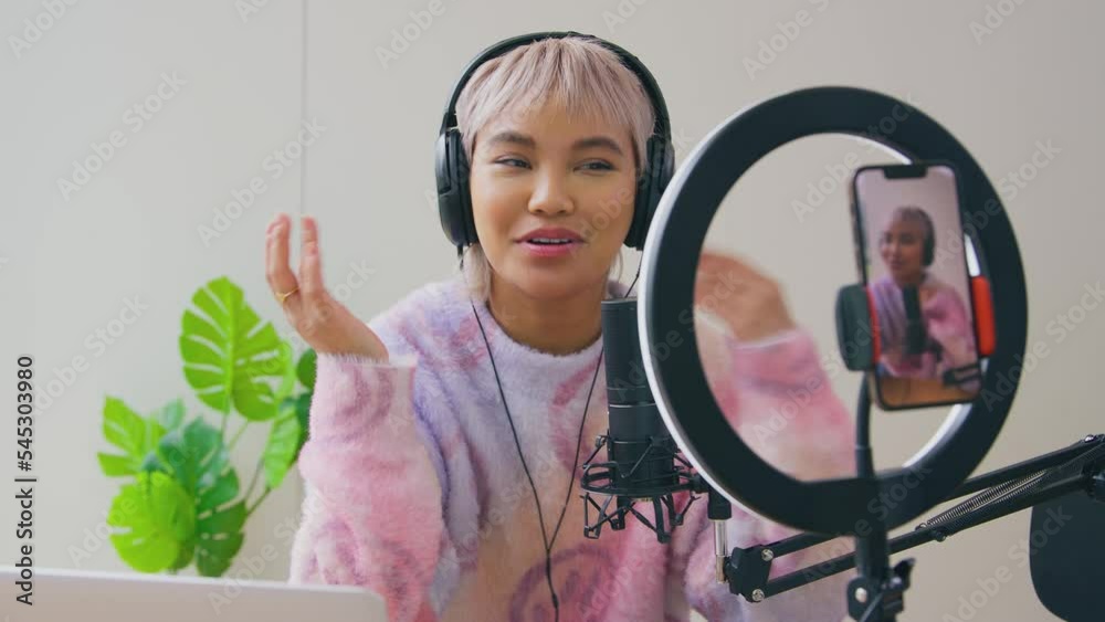 Female vlogger wearing headphones live streaming podcast looking on mobile phone - shot in slow motion