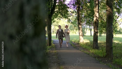 Wallpaper Mural Handheld footage beautiful couple of bride and groom are walking forward through park on sunny summer evening in forest. man in suit and woman in white dress with flowers are walking in park at dawn. Torontodigital.ca