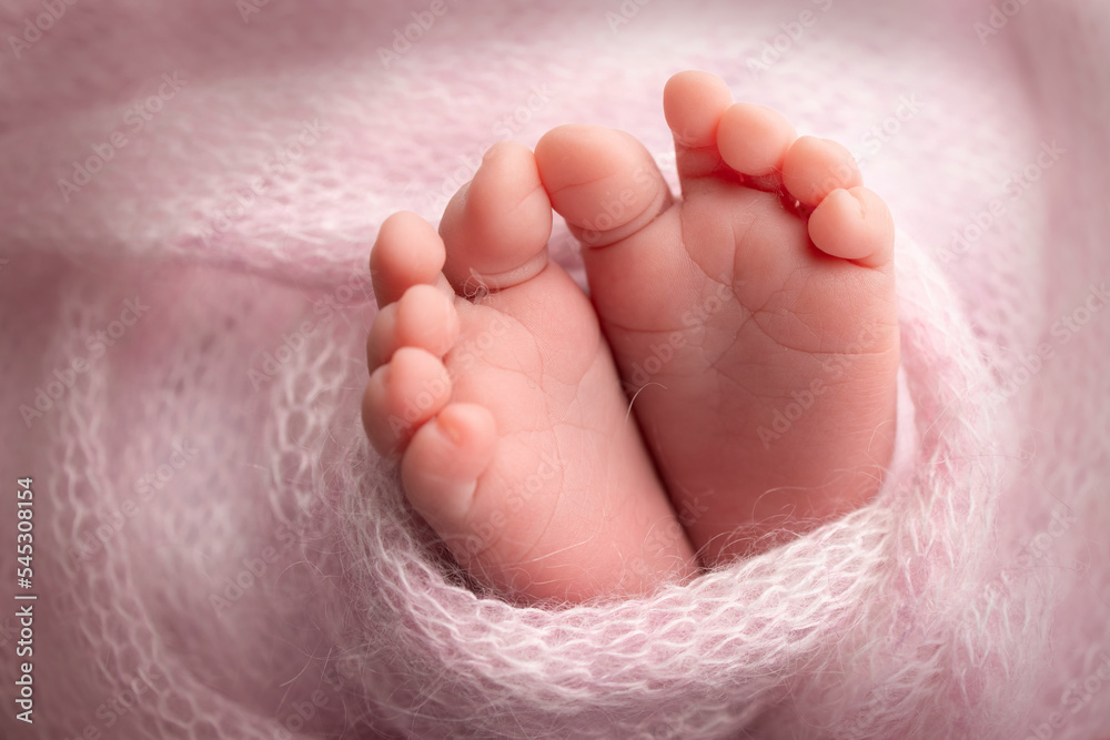 Knitted pink heart in the legs of a baby. Soft feet of a new born in a pink wool blanket. Close-up of toes, heels and feet of a newborn. Macro photography the tiny foot of a newborn baby.