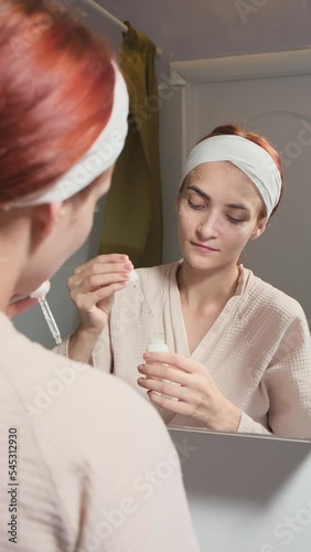 Beauty Day. A woman who takes care of her skin daily in the bathroom in front of a mirror, gently apply anti-aging collagen serum to her face and neck. The concept of beauty, self-care, cosmetics