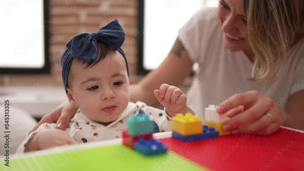 Woman and toddler playing with construction blocks sitting on table at kindergarten Woman and toddler playing with construction blocks sitting on table at kindergarten
