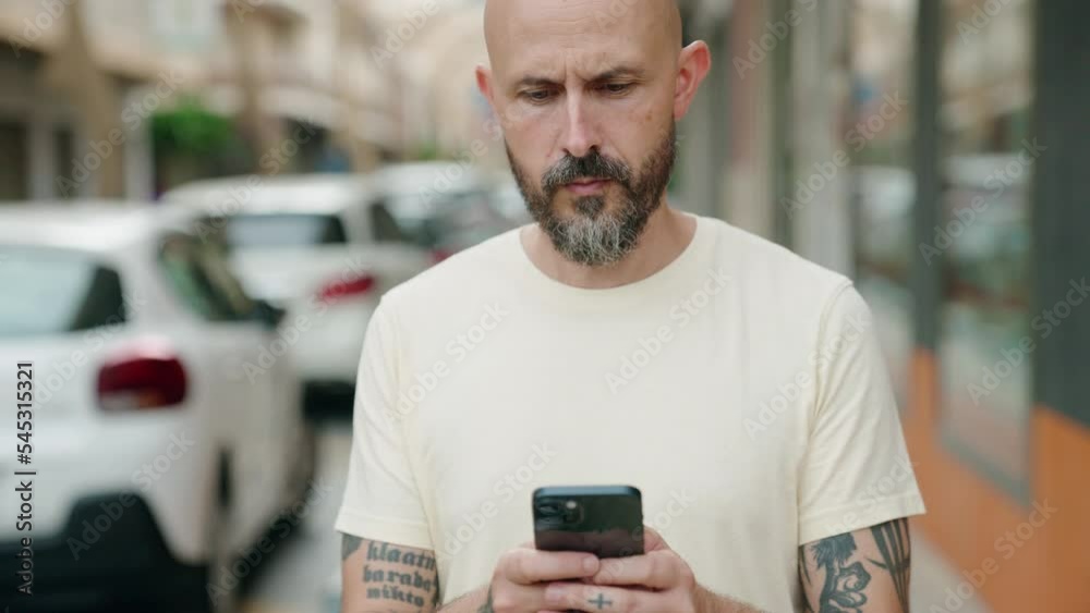 Young bald man using smartphone with serious expression at street Young bald man using smartphone with serious expression at street