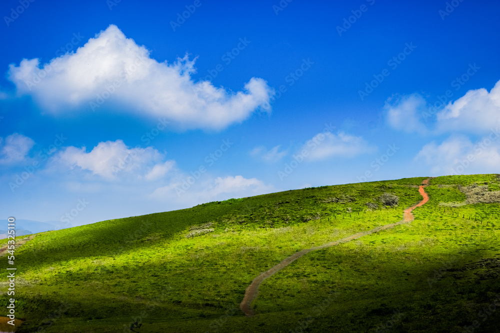 Beautiful rolling hills with winding rugged footpath, and fluffy clouds rolling over the blue sky.