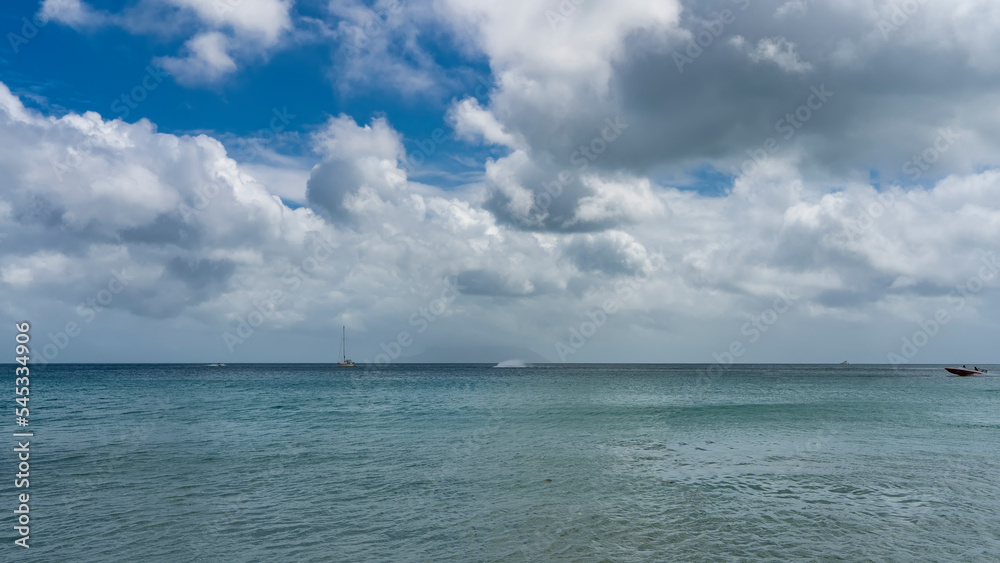 Serene seascape. The turquoise ocean is calm. Yachts and boats are visible on the horizon. Clouds in the blue sky. Seychelles.