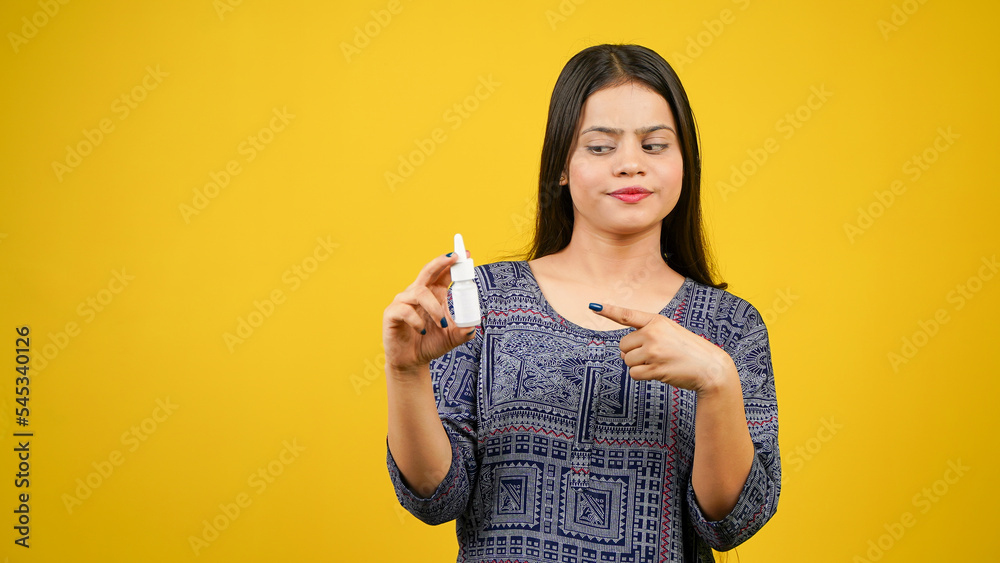 Beautiful young woman holding ear, nose or eyes drop bottle isolated over yellow background Beautiful young woman holding ear, nose or eyes drop bottle isolated over yellow background