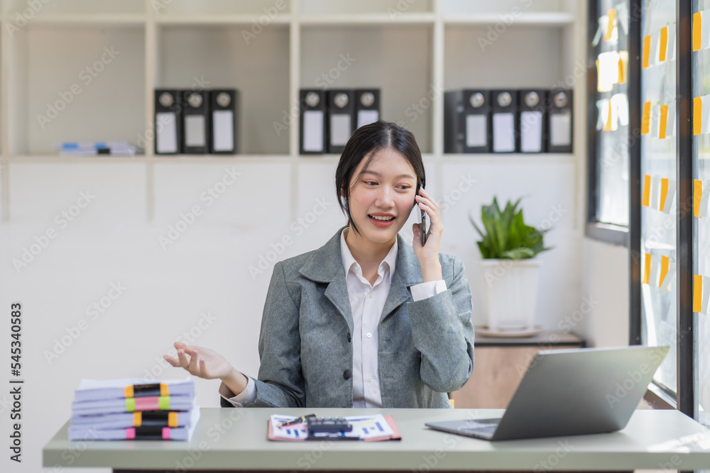Smiling Asian business woman at work Call phone and working on laptop sitting at her working place in office, cheerful woman feel Excited and happy, copy space. Smiling Asian business woman at work Call phone and working on laptop sitting at her working place in office, cheerful woman feel Excited and happy, copy space.