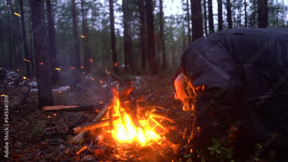 Young bearded man kindles a fire. Campfire in the forest. Beautiful landscape of nature and trees. Sparks and flames. Rest by the fire. Camping in the woods. Burning firewood. Evening bonfire. Young bearded man kindles a fire. Campfire in the forest. Beautiful landscape of nature and trees. Sparks and flames. Rest by the fire. Camping in the woods. Burning firewood. Evening bonfire.