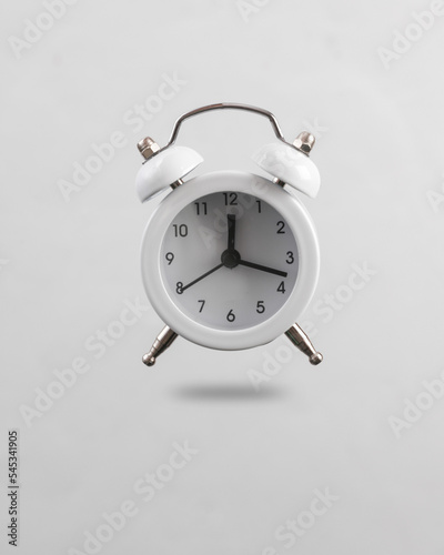 White alarm clock levitating on gray background with shadow