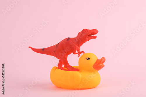 Toy red dinosaur tyrannosaurus rex with rubber duck on pink background. Minimalism creative layout photo