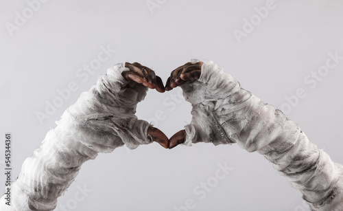 Fototapeta Naklejka Na Ścianę i Meble -  Mummy hands with folded fingers in the shape of a heart on a gray background
