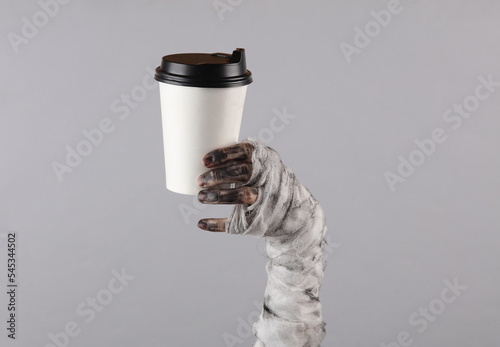 Mummy hand holding coffee cup isolated on gray background. Halloween concept