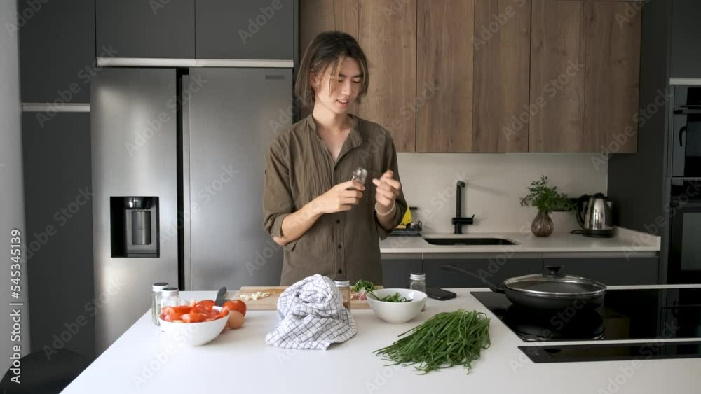 Smiling asian young man checking recipe spices and taking photos at kitchen. Smiling asian young man checking recipe spices and taking photos at kitchen.