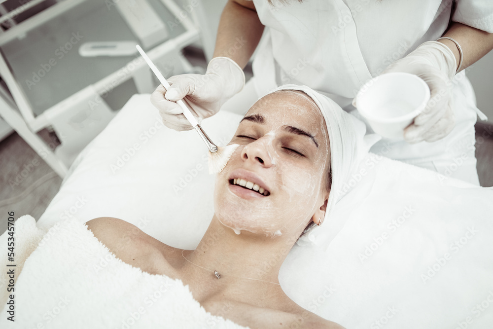 Cosmetological procedures. Beauty salon, doctor in gloves touching face of beautiful woman with closed eyes with brush.