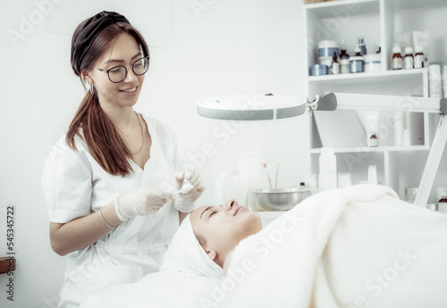 Cute woman beautician makes a cosmetic procedure to a patient in a beauty salon. Facial skin care