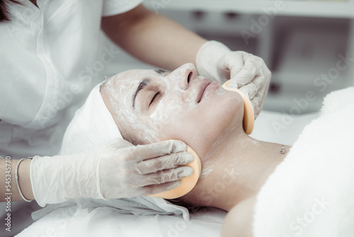 Facial massage and skincare treatment. Dermatologist hands cleaning relaxed serene young woman face with pads in beauty salon during skincare treatment. Face massage