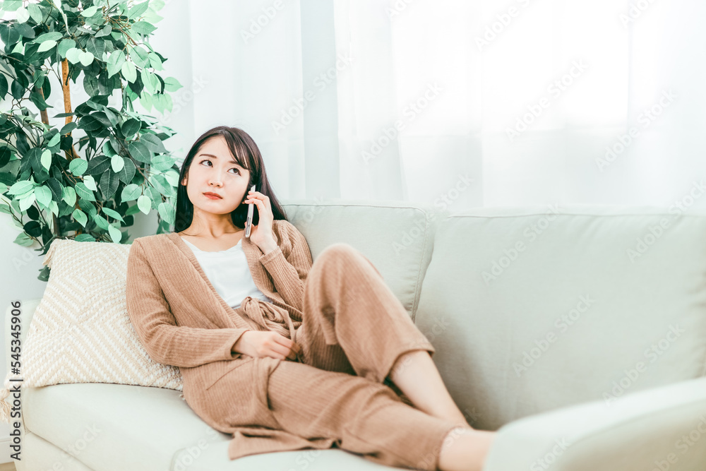 家のソファでスマホで電話する日本人女性
家のソファでスマホで電話する日本人女性