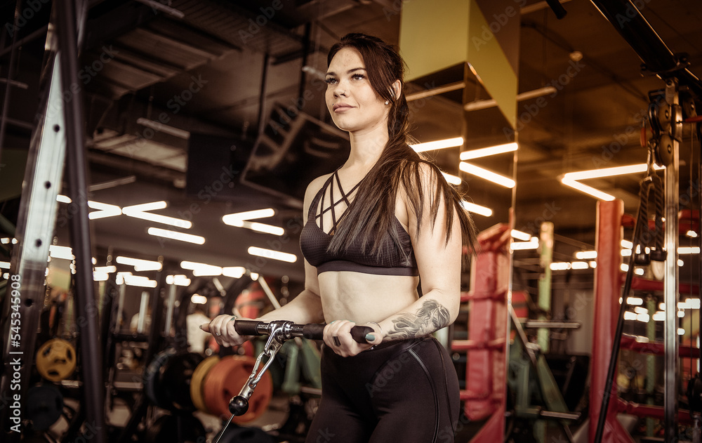 Fitness woman trains biceps in crossover cable exercise machine in modern gym Fitness woman trains biceps in crossover cable exercise machine in modern gym