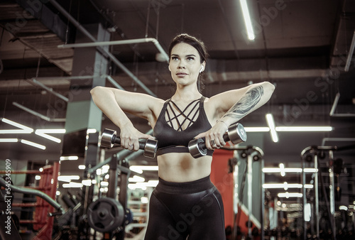 Young fitness woman practicing chin dumbbell rows in the gym