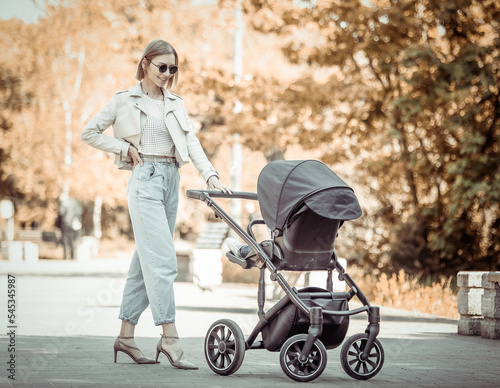 Young stylish mom in sunglasses walking with stroller in the park