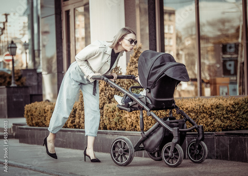 Stylish loving mom walks with a stroller in the city location. Maternity, lifestyle photo