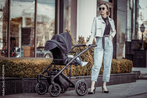 Stylish loving mom walks with a stroller in the city location. Maternity, lifestyle