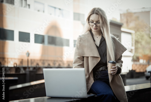 Business woman uses laptop and holds a cup of coffee in urban location. Distant, online work Free Download Business woman uses laptop and holds a cup of coffee in urban location. Distant, online work - GFXLoad