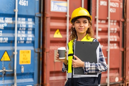 Young professional caucasian cargo inspector holding a cup of coffee while checking cargo containers in a shipping containers yard