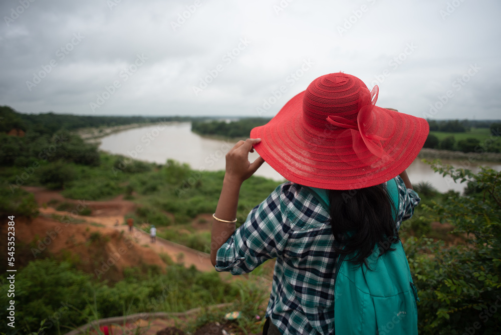 Backside of a woman in red hat in front of a river bed