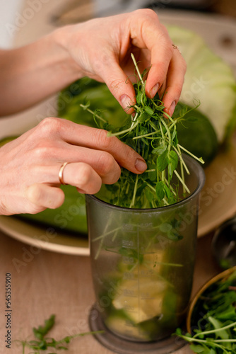 A woman cooking a smoothie from micro-greens and vegetables at home in the kitchen, hands close-up.Healthy eating and healthy lifestyle.Cooking at home. Vegetarian and vegan diet.Veganuary concept.