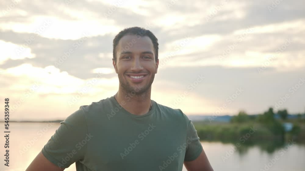 Close up portrait of handsome young cheerful sportsman standing on nature outdoors looking at camera and smiling. African American attractive male athlete standing on lake on sunset Close up portrait of handsome young cheerful sportsman standing on nature outdoors looking at camera and smiling. African American attractive male athlete standing on lake on sunset