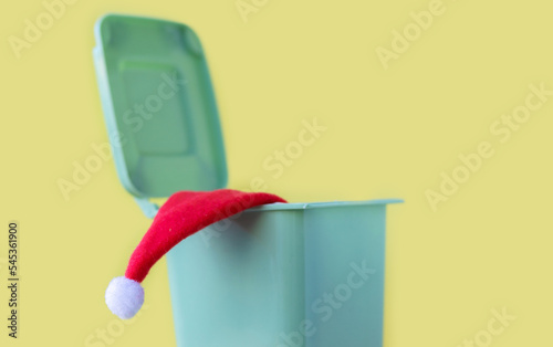 red color small lsanta cap hat throw away dropped off in mini trash bin can garbage waste.christmas holiday is over or against celebration.santa claus robe clothes happy new year isolated yellow 