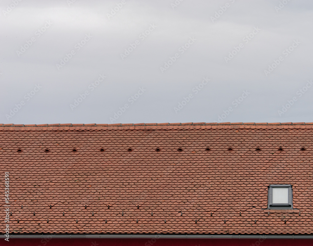 Naklejka premium Close-up photo of a red roof tile with one window and a bright sky in the background