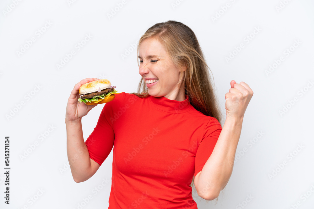Young blonde woman holding a burger isolated on white background celebrating a victory Young blonde woman holding a burger isolated on white background celebrating a victory