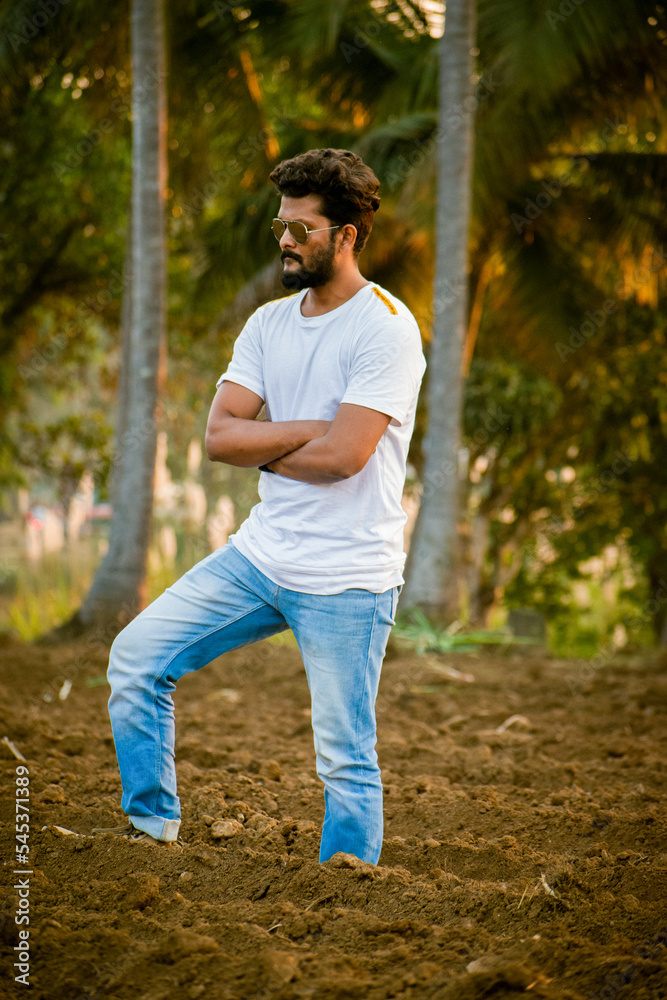 Handsome Indian guy with beard and sunglasses standing at the field, with closed arms.