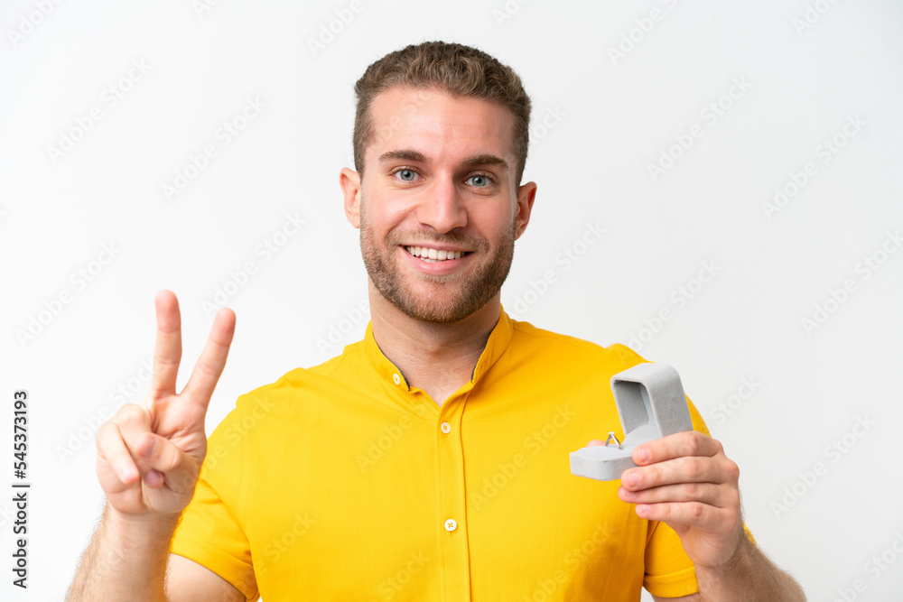 Young man holding a engagement ring isolated on white background smiling and showing victory sign Young man holding a engagement ring isolated on white background smiling and showing victory sign